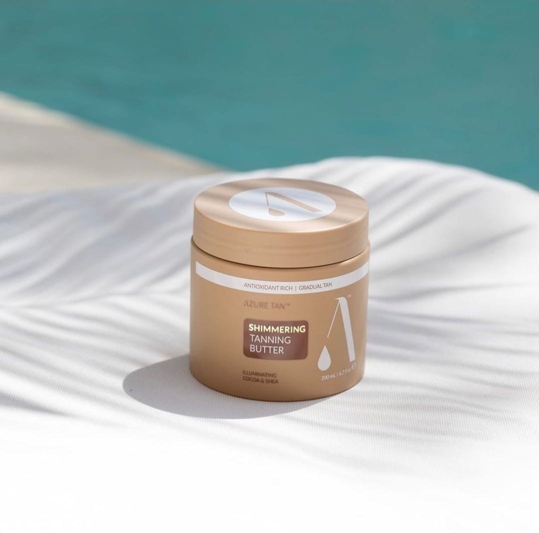 Jar of shimmering tanning butter on a white surface with a blue background