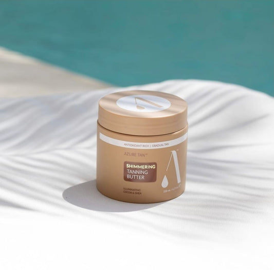 Jar of shimmering tanning butter on a white surface with a blue background