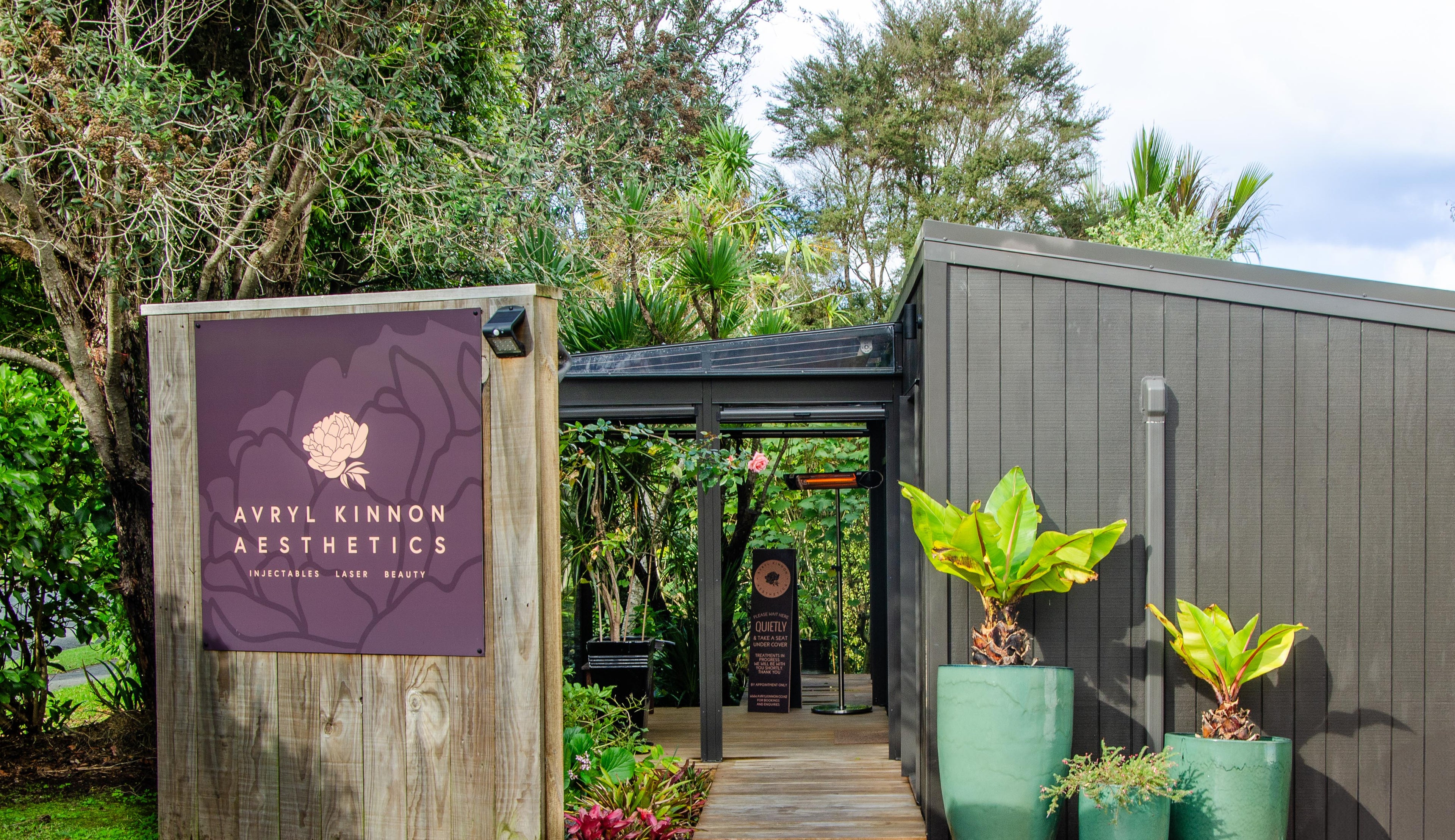 Entrance to Avyl Kinnon Aesthetics with a sign and potted plants.