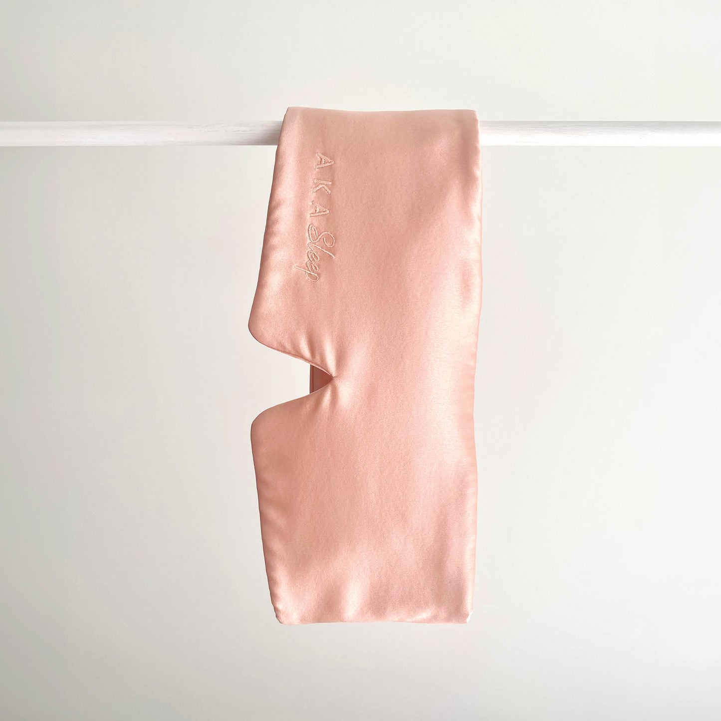 Blush Pink 100% Mulberry Silk Deep Sleep Eye Mask handing on a white rod with a white background