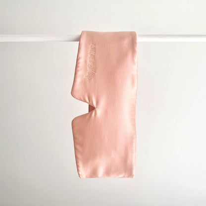 Blush Pink 100% Mulberry Silk Deep Sleep Eye Mask handing on a white rod with a white background