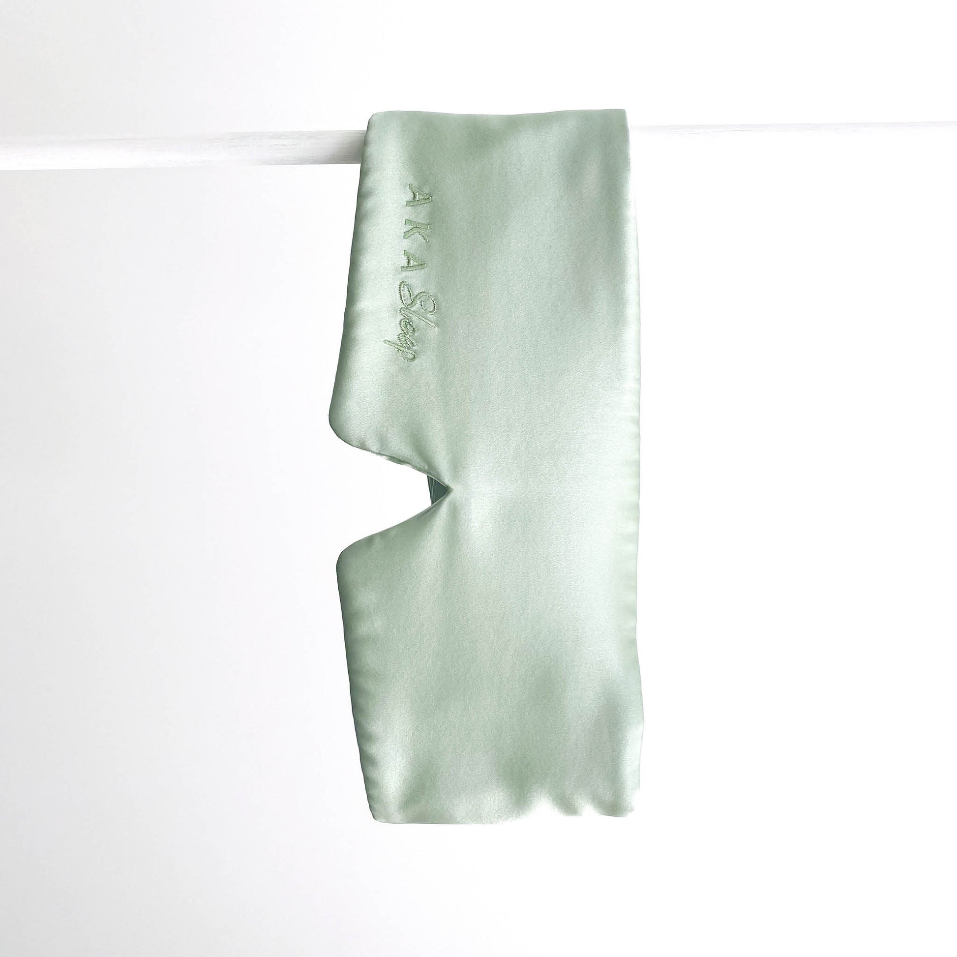 Sage green 100% Mulberry Silk AKA Sleep Deep Sleep Eye Mask hanging on a white rod in front of a white background